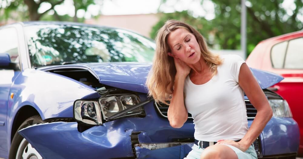 A woman is sitting after a car accident, her neck hurting.